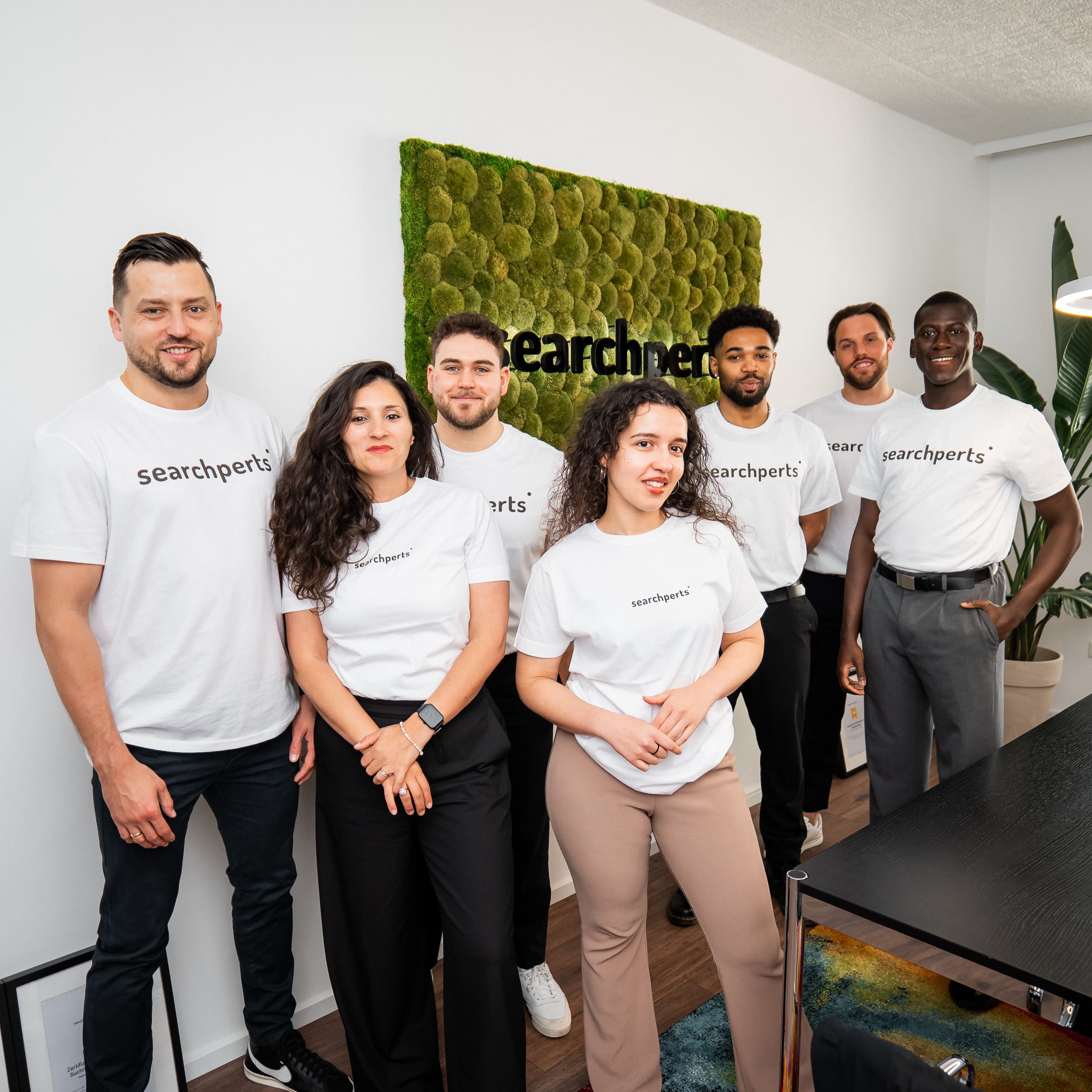 Das Team von Searchperts stehen zusammen im Düsseldorfer Büro. Alle tragen weiße T-Shirts mit dem Firmenlogo.
